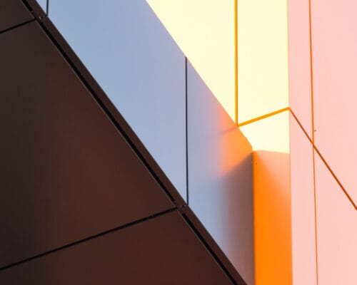 Geometric color elements of the building facade with planes, lines, corners with highlights and reflections for an abstract background and texture of gray, orange colors. Place for text