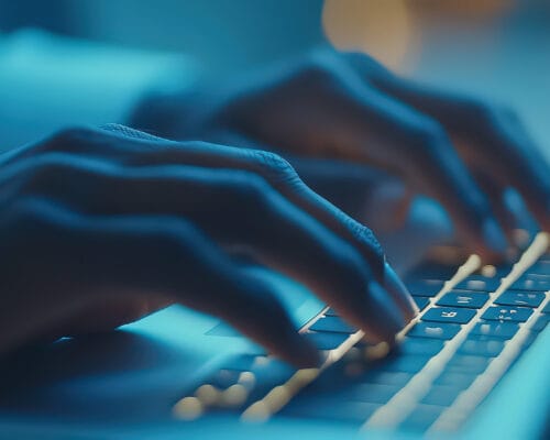 Close-up of hands typing on an illuminated laptop keyboard, sho